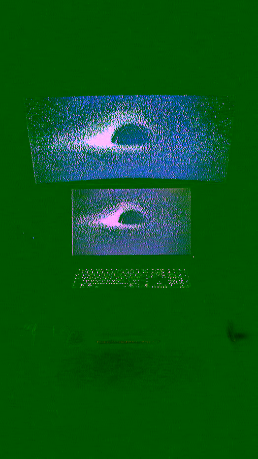 Two screen workstation with a Dell P2214H monitor on the desk and a larger curved Samsung ViewFinity S65UA monitor mounted above, both showing the same grainy blue and purple edit of the Jean-Pierre Luminet black hole image; Logitech MX Keys S Keyboard backlight is visible; dark, moody room with low ambient lighting; tone is contemplative and cinematic